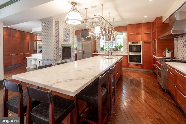 kitchen with premium appliances, a breakfast bar area, dark wood-type flooring, a fireplace, and wall chimney exhaust hood