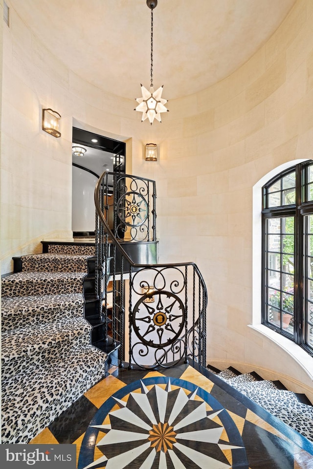 staircase with tile walls and an inviting chandelier