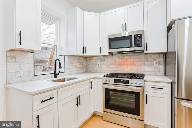 kitchen featuring stainless steel appliances, white cabinets, a sink, and light stone countertops