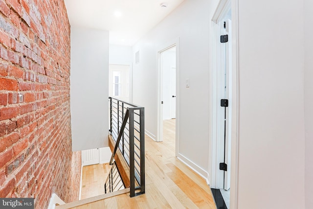 hallway with brick wall, visible vents, an upstairs landing, baseboards, and light wood-type flooring