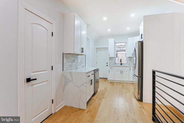 kitchen featuring light stone countertops, white cabinets, light wood-style floors, appliances with stainless steel finishes, and decorative backsplash