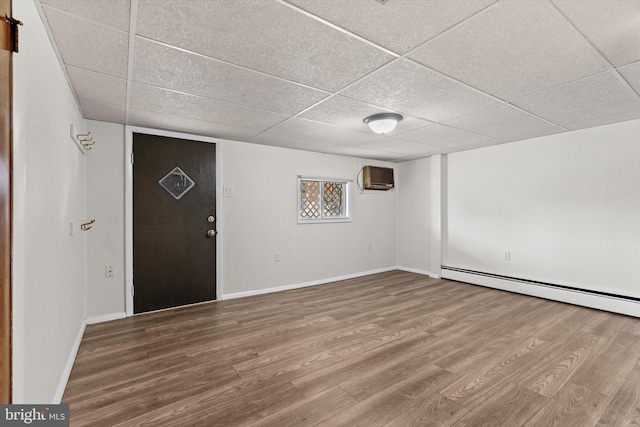 interior space with a paneled ceiling, a baseboard radiator, an AC wall unit, and wood finished floors