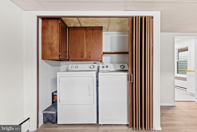 laundry room with light wood-type flooring, cabinet space, baseboard heating, and washing machine and clothes dryer