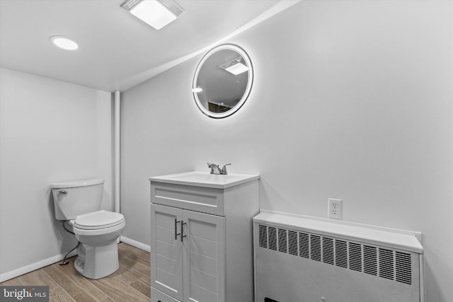 bathroom with toilet, wood finished floors, vanity, baseboards, and radiator heating unit