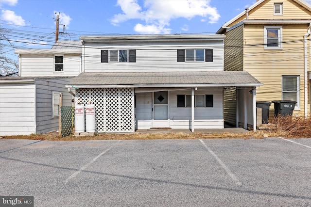 view of front of property featuring a porch, uncovered parking, and a shingled roof