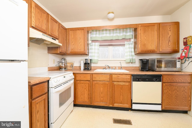 kitchen featuring under cabinet range hood, light floors, light countertops, white appliances, and a sink