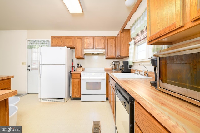 kitchen featuring visible vents, a sink, under cabinet range hood, white appliances, and light floors