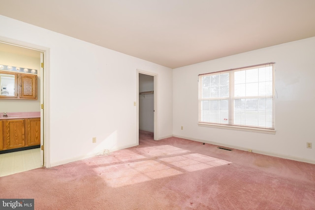 unfurnished bedroom featuring connected bathroom, baseboards, light colored carpet, and visible vents