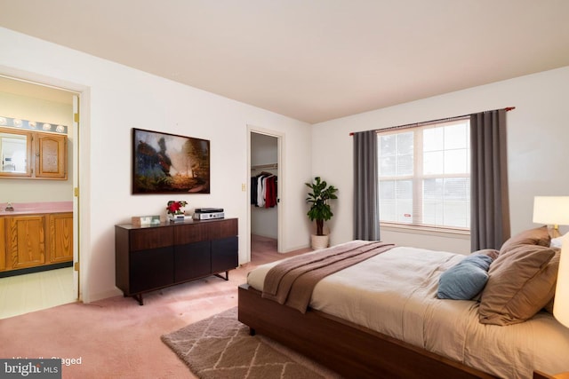 bedroom featuring a walk in closet, light carpet, a sink, ensuite bath, and a closet