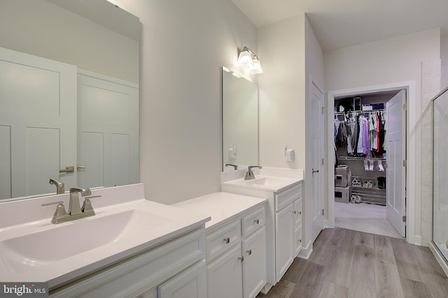 bathroom featuring a shower stall, a walk in closet, wood finished floors, and vanity