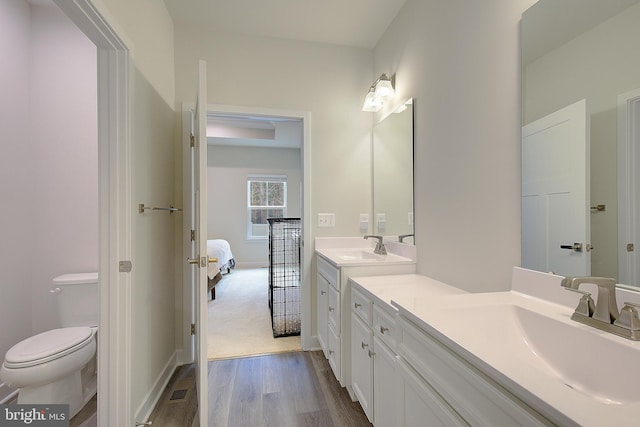 ensuite bathroom featuring connected bathroom, toilet, wood finished floors, vanity, and baseboards