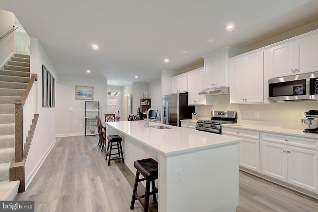 kitchen with an island with sink, a kitchen breakfast bar, stainless steel appliances, under cabinet range hood, and a sink