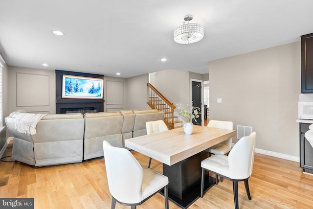 dining room featuring a fireplace, visible vents, baseboards, stairs, and light wood finished floors