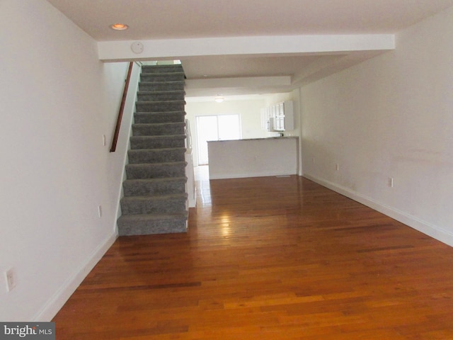 empty room with recessed lighting, wood finished floors, baseboards, and stairs