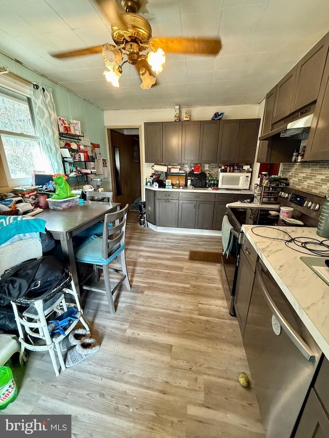 kitchen featuring a ceiling fan, light wood-style flooring, stainless steel appliances, decorative backsplash, and light countertops