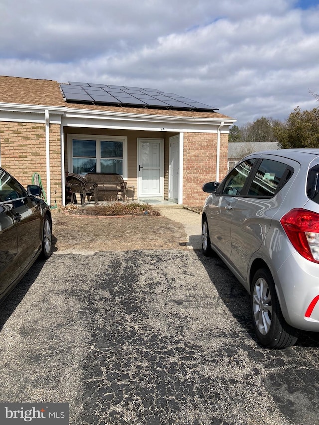 exterior space with brick siding, roof mounted solar panels, a porch, and uncovered parking