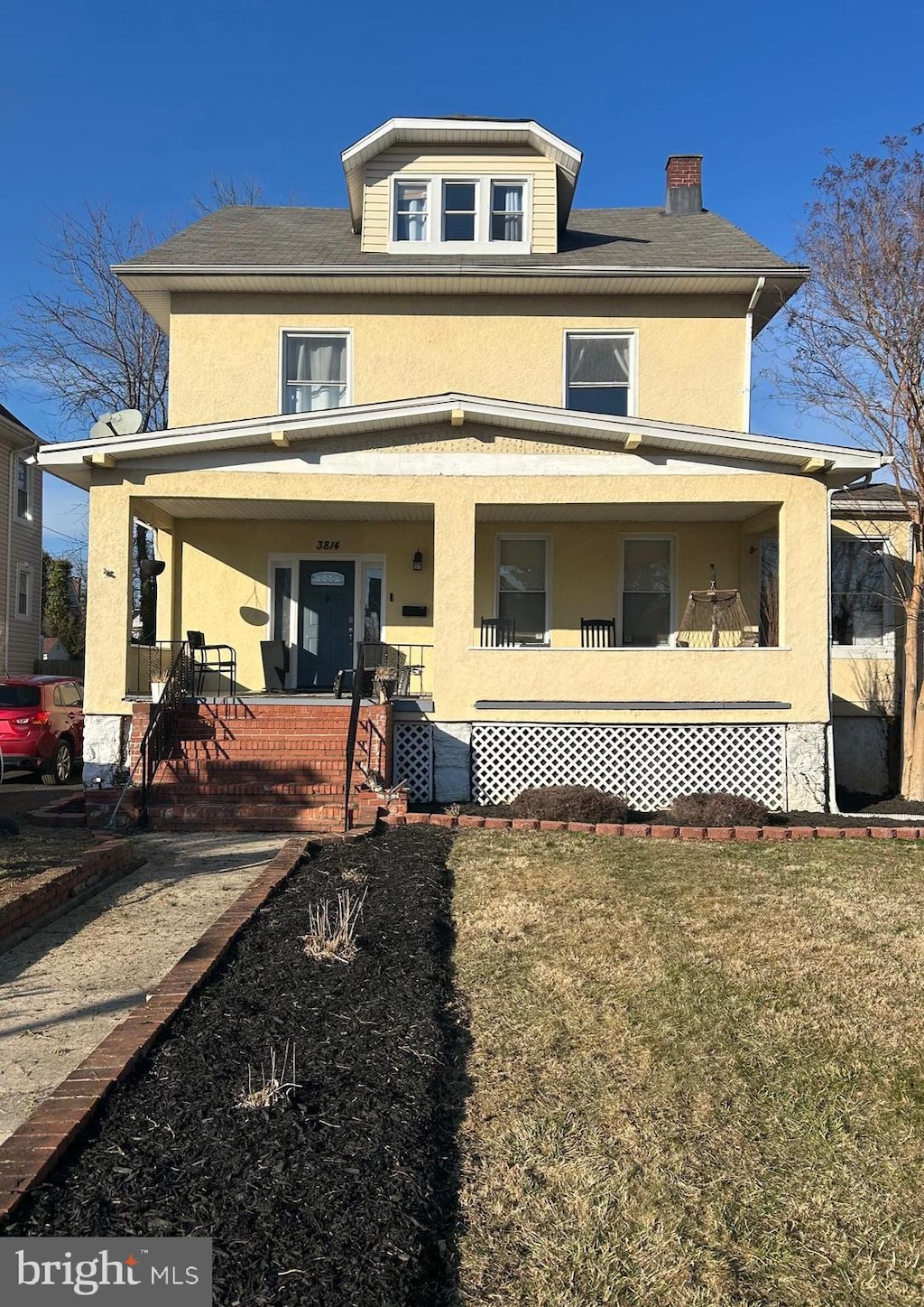 american foursquare style home featuring covered porch, a front lawn, and stucco siding