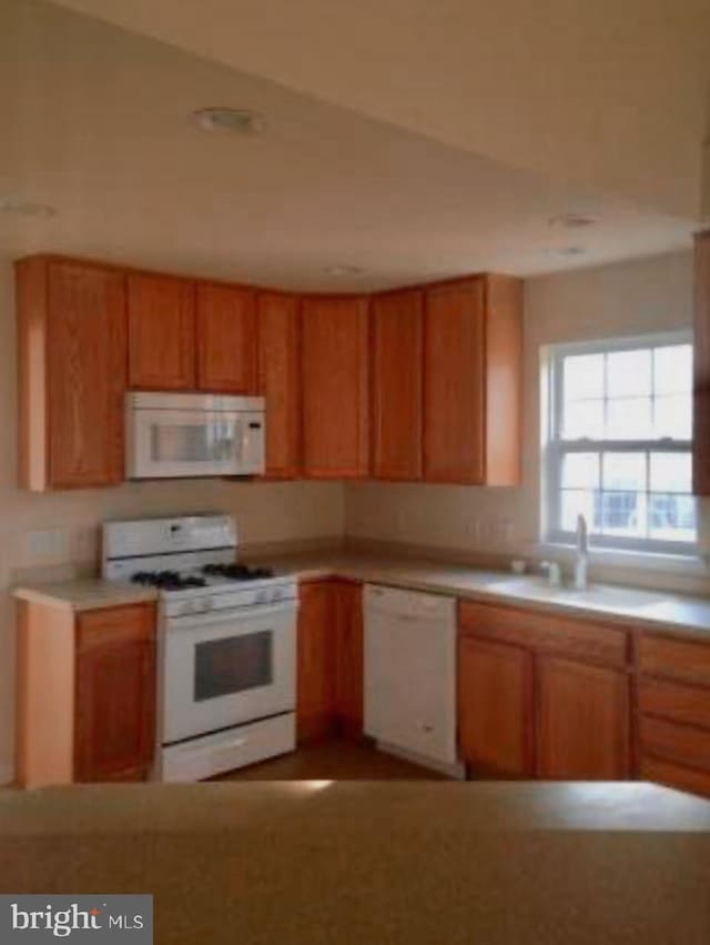 kitchen featuring brown cabinets, white appliances, light countertops, and a sink