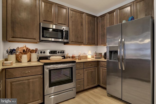 kitchen featuring stainless steel appliances, light countertops, dark brown cabinetry, and light wood-style flooring