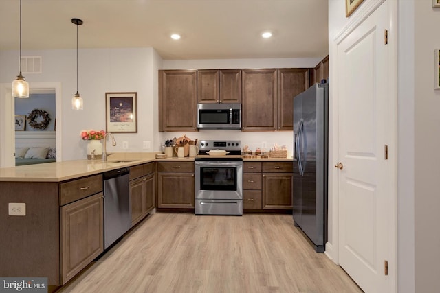 kitchen with visible vents, a peninsula, stainless steel appliances, light wood-type flooring, and a sink