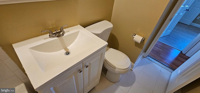 half bath with baseboards, vanity, toilet, and tile patterned floors