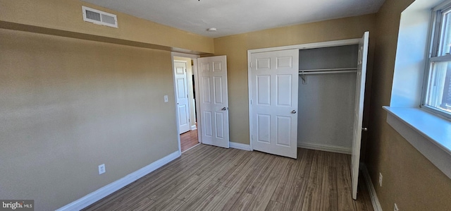 unfurnished bedroom featuring baseboards, a closet, visible vents, and wood finished floors