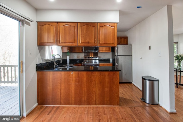 kitchen featuring a peninsula, appliances with stainless steel finishes, brown cabinetry, and a sink