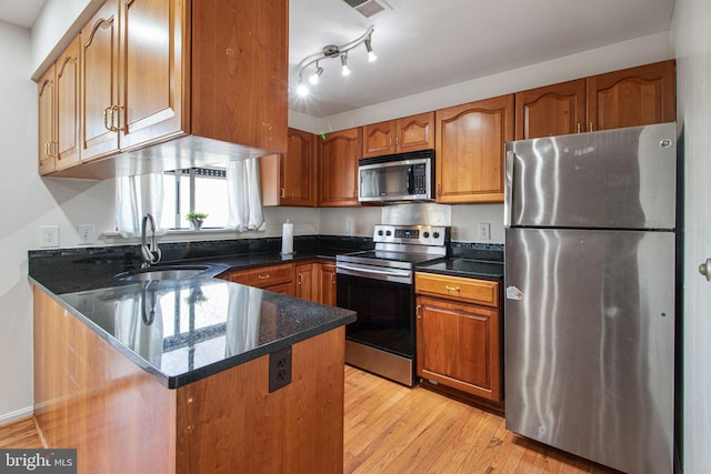 kitchen featuring appliances with stainless steel finishes, brown cabinets, a sink, and a peninsula