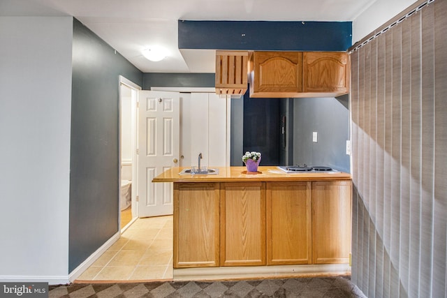 kitchen with light tile patterned floors, baseboards, a peninsula, stainless steel cooktop, and a sink