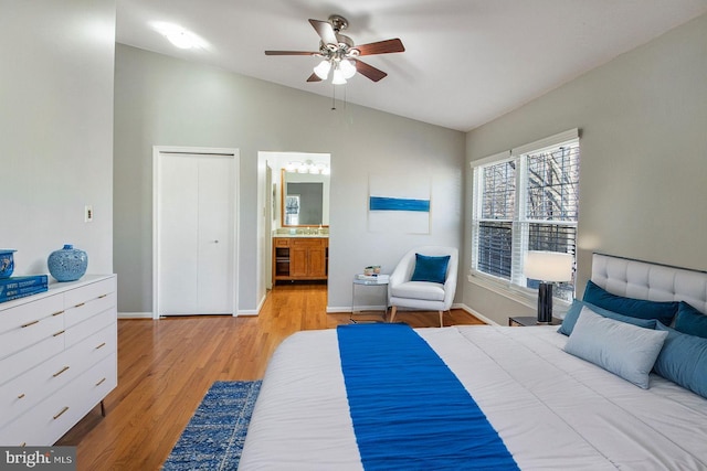 bedroom featuring baseboards, ensuite bathroom, vaulted ceiling, light wood-type flooring, and a sink