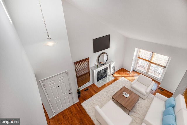 living area with high vaulted ceiling, a fireplace with flush hearth, visible vents, and wood finished floors