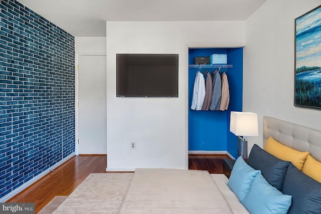 bedroom featuring baseboards, brick wall, an accent wall, wood finished floors, and a closet