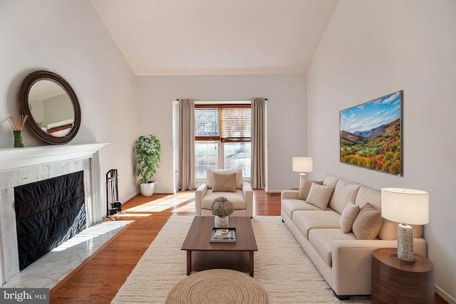 living room with light wood-style flooring, a fireplace, baseboards, and vaulted ceiling