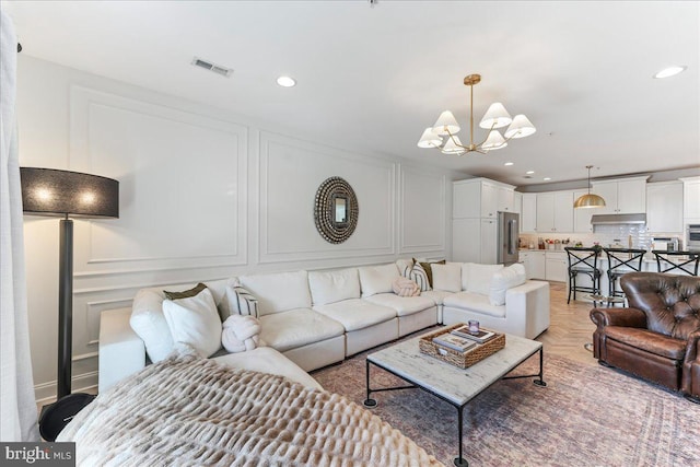 living area featuring visible vents, a decorative wall, a notable chandelier, and recessed lighting