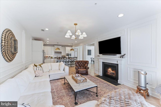 living area with a chandelier, a decorative wall, a fireplace with flush hearth, and recessed lighting