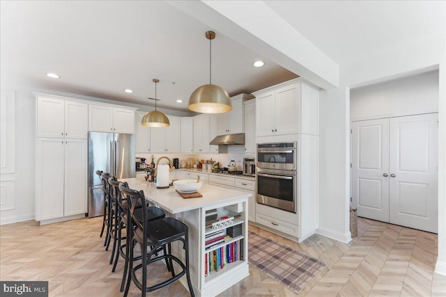 kitchen with a breakfast bar area, under cabinet range hood, white cabinetry, light countertops, and appliances with stainless steel finishes