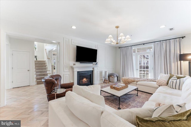 living area featuring recessed lighting, visible vents, a glass covered fireplace, a chandelier, and stairs