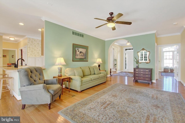 living room featuring baseboards, light wood-type flooring, visible vents, and crown molding