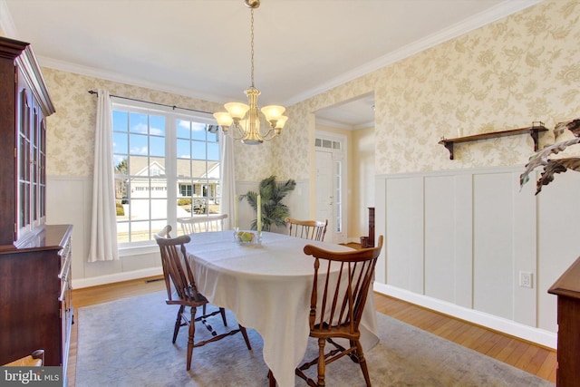 dining area featuring ornamental molding, wood finished floors, wainscoting, and wallpapered walls