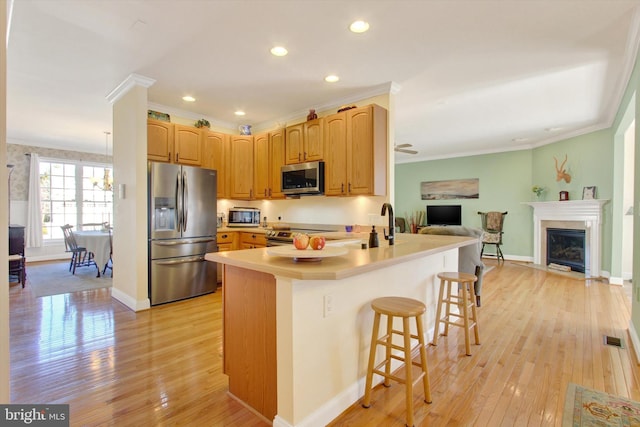 kitchen featuring stainless steel appliances, ornamental molding, light wood-type flooring, and a peninsula