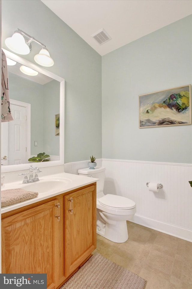 bathroom with a wainscoted wall, visible vents, toilet, vanity, and tile patterned floors