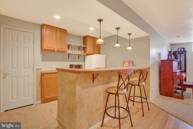 kitchen with a breakfast bar area, baseboards, hanging light fixtures, freestanding refrigerator, and open shelves