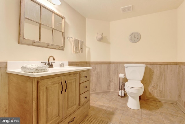 bathroom with wainscoting, wood walls, visible vents, and toilet