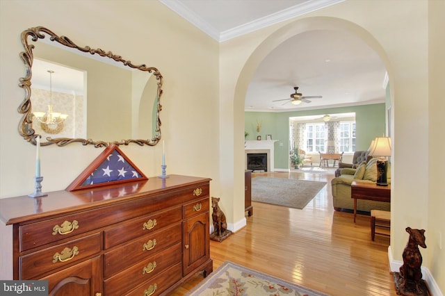 hallway featuring light wood-style floors, arched walkways, a notable chandelier, and crown molding