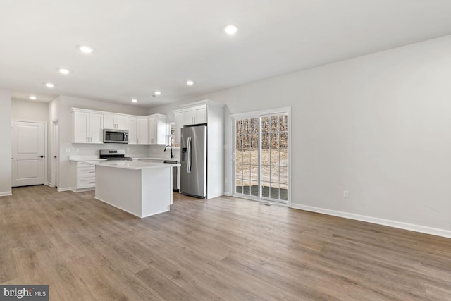 kitchen with light countertops, appliances with stainless steel finishes, a kitchen island, and light wood-style floors