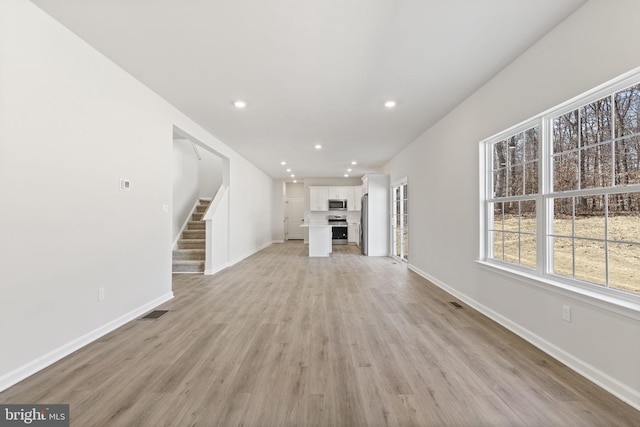 unfurnished living room with recessed lighting, visible vents, light wood-type flooring, baseboards, and stairs