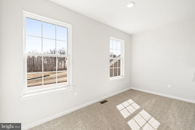 carpeted spare room with a healthy amount of sunlight, baseboards, and visible vents