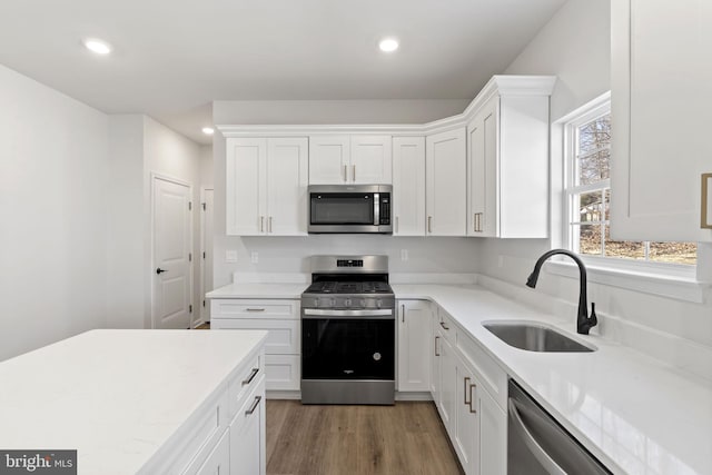 kitchen with appliances with stainless steel finishes, light wood-type flooring, white cabinetry, a sink, and recessed lighting