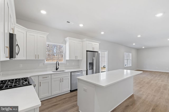 kitchen with stainless steel appliances, a kitchen island, a sink, visible vents, and open floor plan