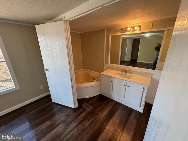 full bath with a textured ceiling, a garden tub, wood finished floors, visible vents, and vanity